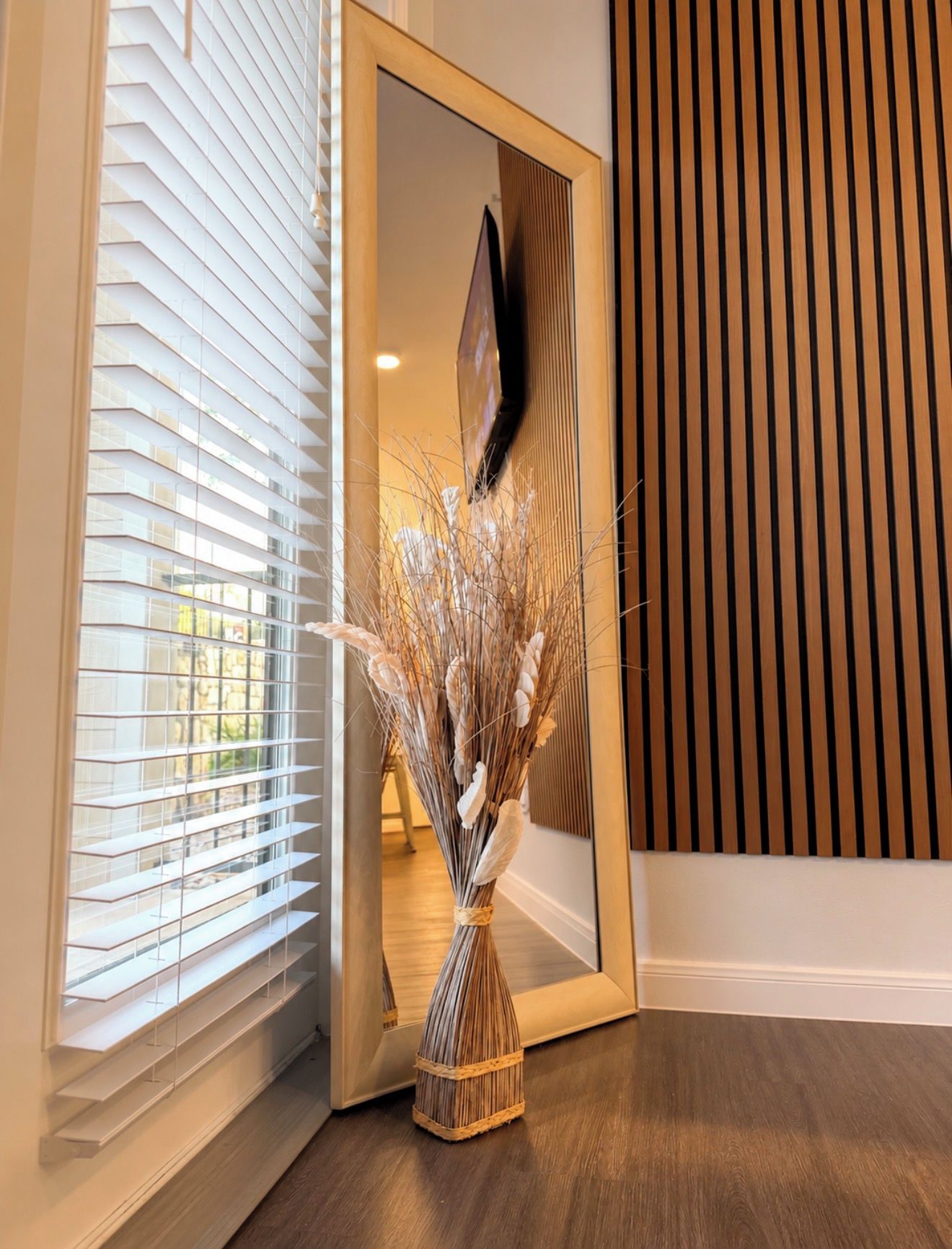 A room with a wooden floor, a mirror, and a window with blinds.