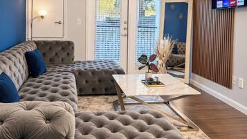 A living room with a sectional sofa, a coffee table, and a television mounted on the wall.