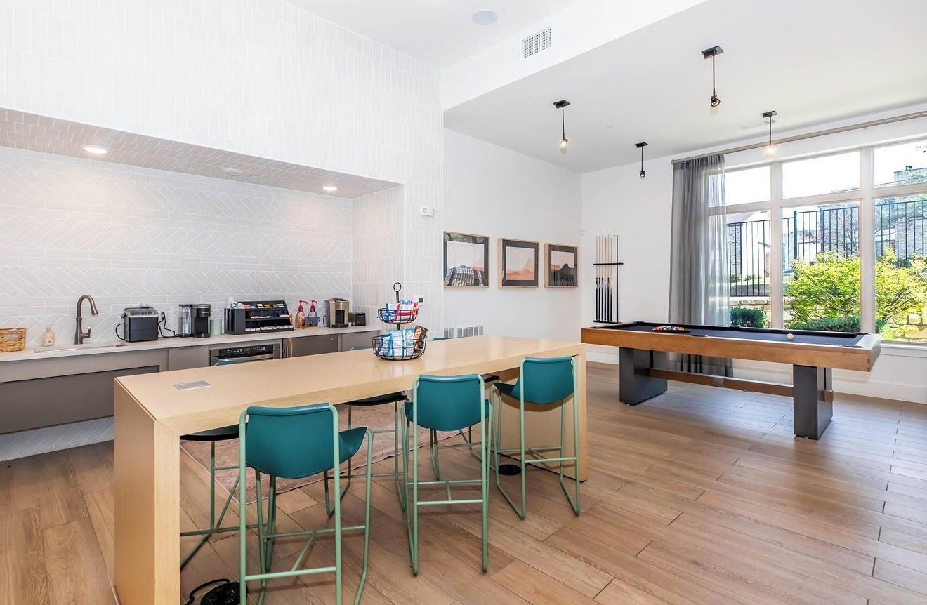 A modern kitchen with a pool table, bar stools, and a dining table.