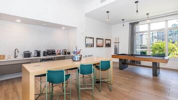 A modern kitchen with a pool table, bar stools, and a dining table.