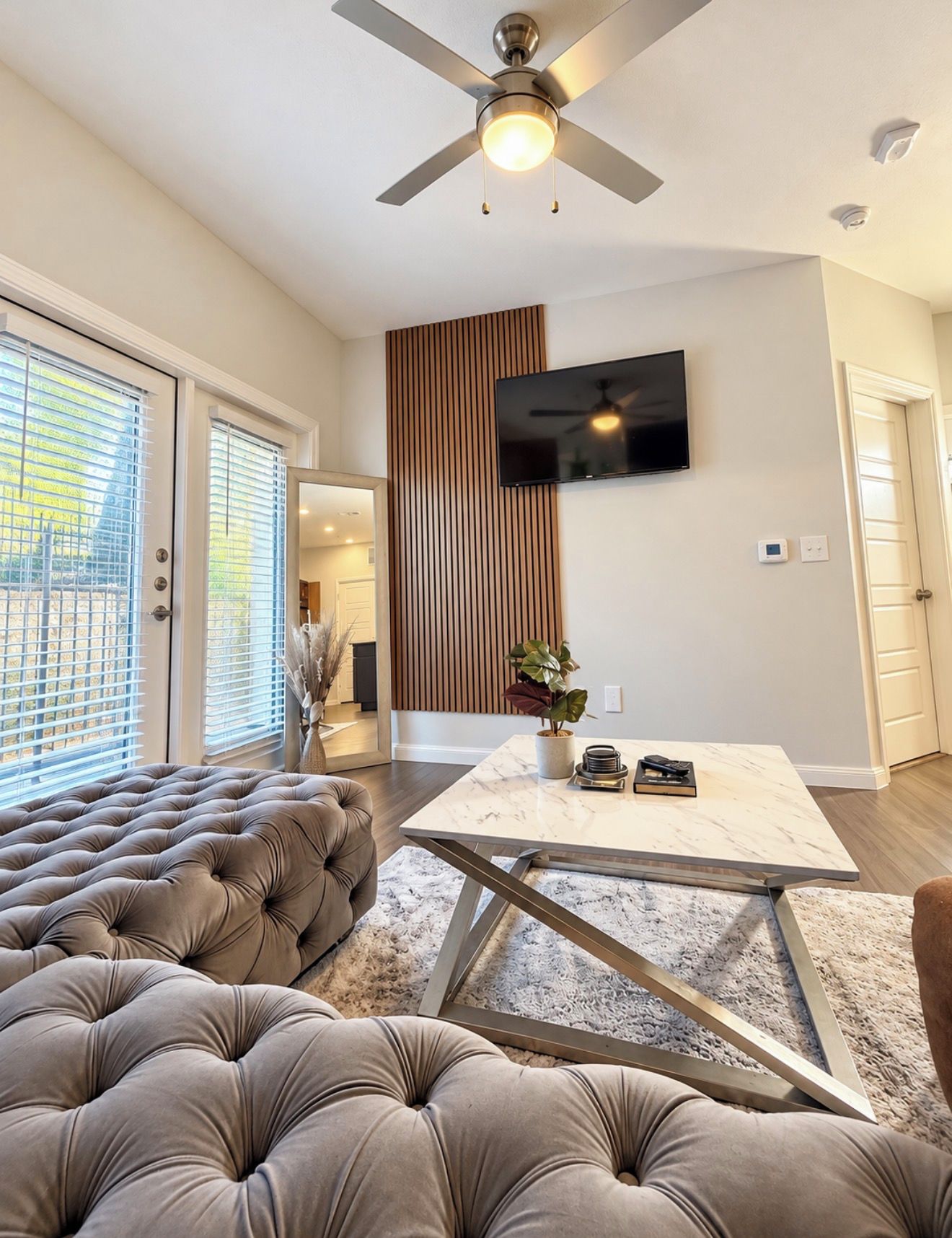 A modern living room with a tufted sofa, a glass coffee table, and a ceiling fan.