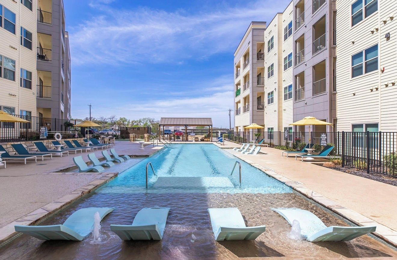A swimming pool with lounge chairs and umbrellas, surrounded by multi-story buildings.