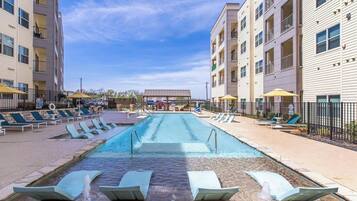 A swimming pool with lounge chairs and umbrellas, surrounded by multi-story buildings.