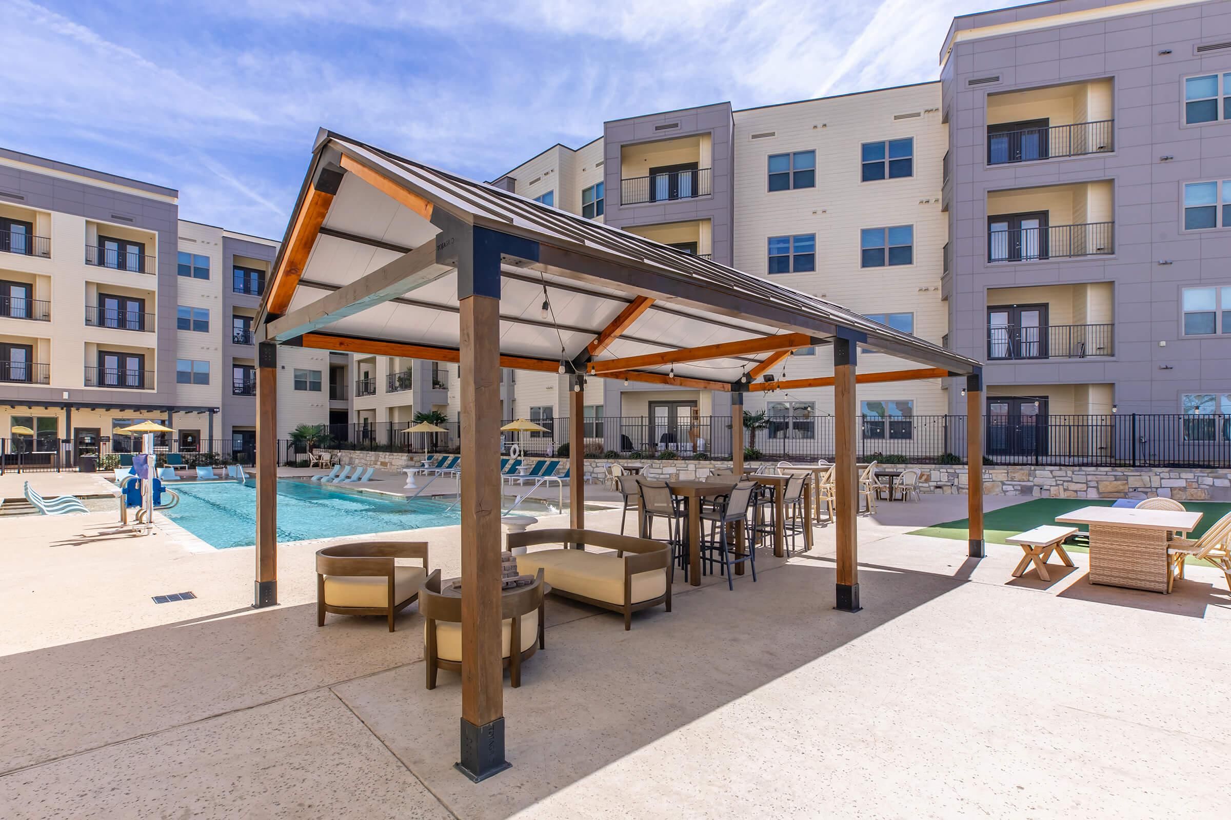 A poolside area with a covered seating area, lounge chairs, and a pool.