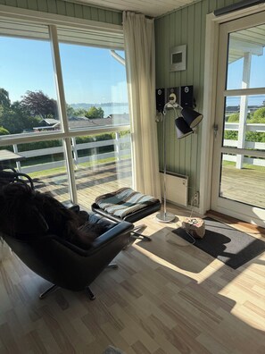 A room with a large window, a black chair, a small table, and a floor lamp. - Holiday home with sea views near the beach (Egernsund)