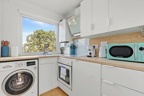 A compact kitchen with a washing machine, microwave, and a view of the outdoors. - The Primrose Loft | Garden Views | Regents Park (Greater London)