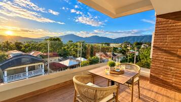 Un balcón con vistas a un paisaje urbano y montañas, con una mesa y dos sillas.