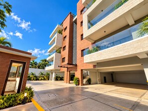 A modern multi-story building with a flat roof, large windows, and a covered outdoor area with a paved floor. - New Listing (Jarabacoa)