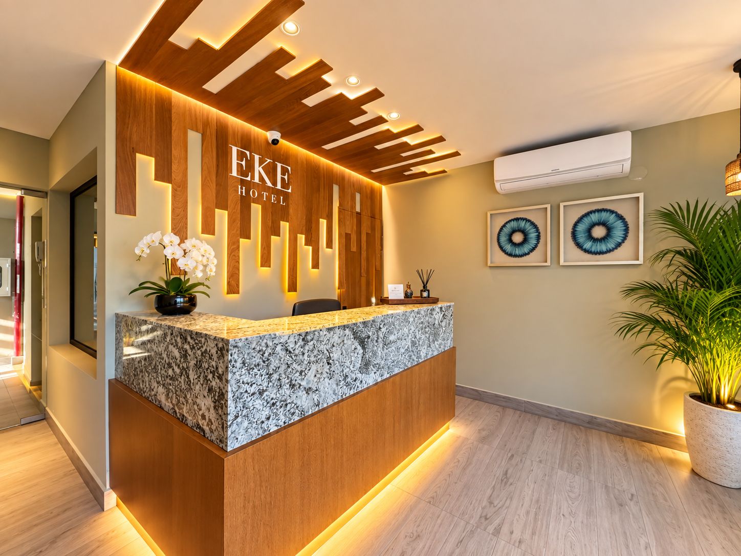 A hotel reception desk with a wooden panel design, a marble counter, and a potted plant.