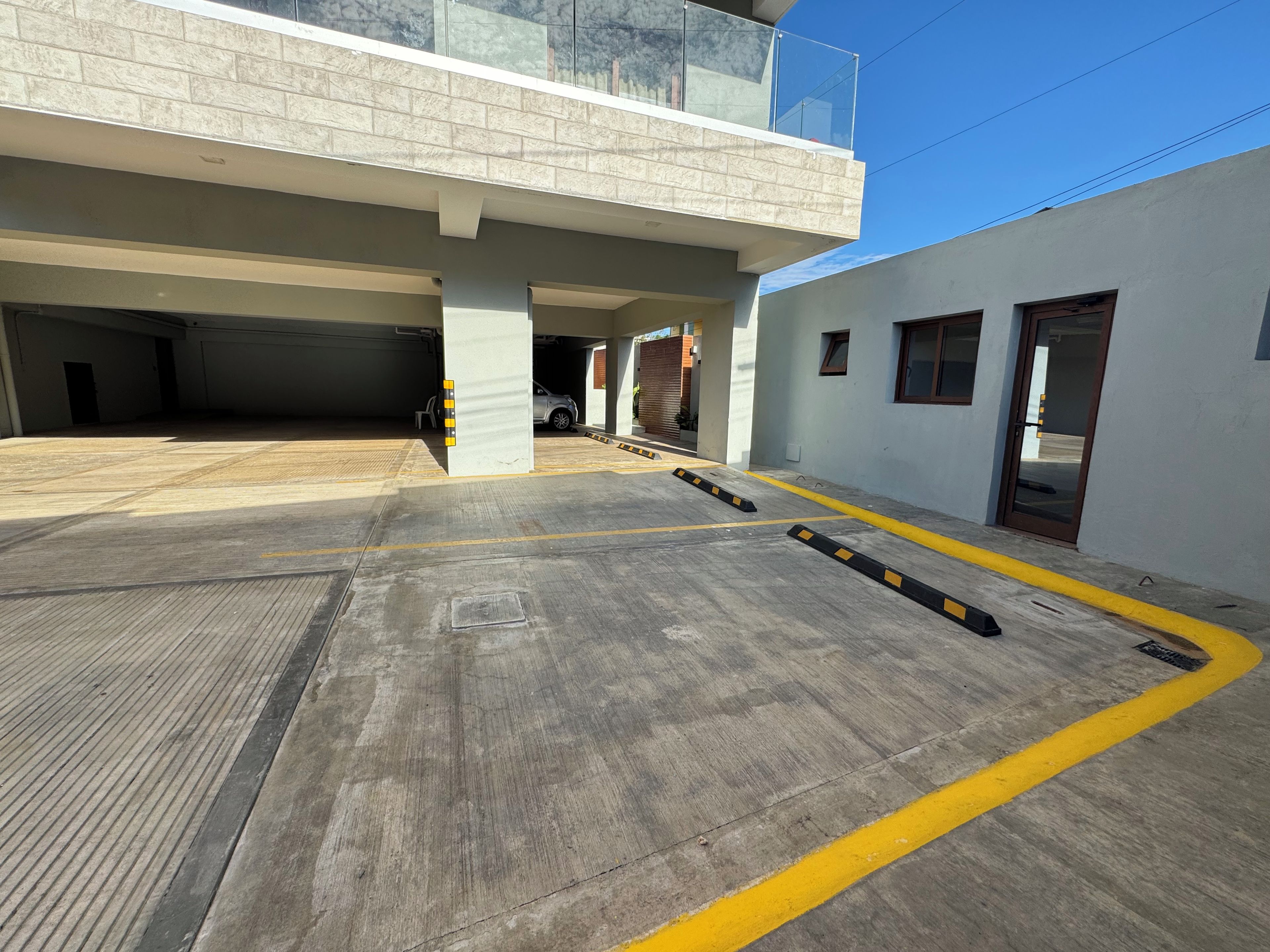 A parking area with marked spaces, a covered section, and a building with a balcony.