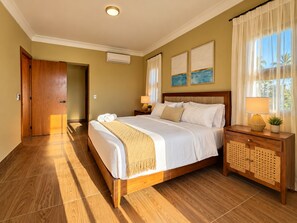 A hotel room with a wooden bed, a nightstand with a lamp, and a view of palm trees through the window. - New Listing (Jarabacoa)