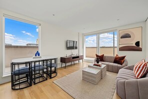 A modern living room with a sofa, coffee table, and a dining area with chairs. - The Masson Terrace | 3-Bed | Parking & Kew Gardens (Greater London)