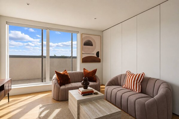 A modern living room with a sofa, armchair, and coffee table, large windows with a view, and minimalist decor. - The Masson Terrace | 3-Bed | Parking & Kew Gardens (Greater London)