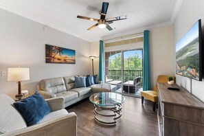 A modern living room with a sofa, a glass coffee table, a TV, and a balcony with a view. - Poolside Stay | Private Balcony | Near Disney (Davenport)