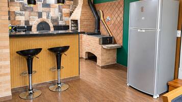 Une cuisine équipée d’un four en briques, de deux tabourets de bar, d’un réfrigérateur en acier inoxydable et d’un éclairage suspendu.