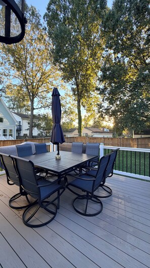 Een terras buiten met een tafel en stoelen, omgeven door een houten hek en bomen.