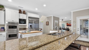 A modern kitchen with granite countertops, stainless steel appliances, and white cabinetry. - Wooded Wonder by Avantstay Game Room + Covered Decks + Fire Pit Near Lake Arrowhead (Lake Arrowhead)