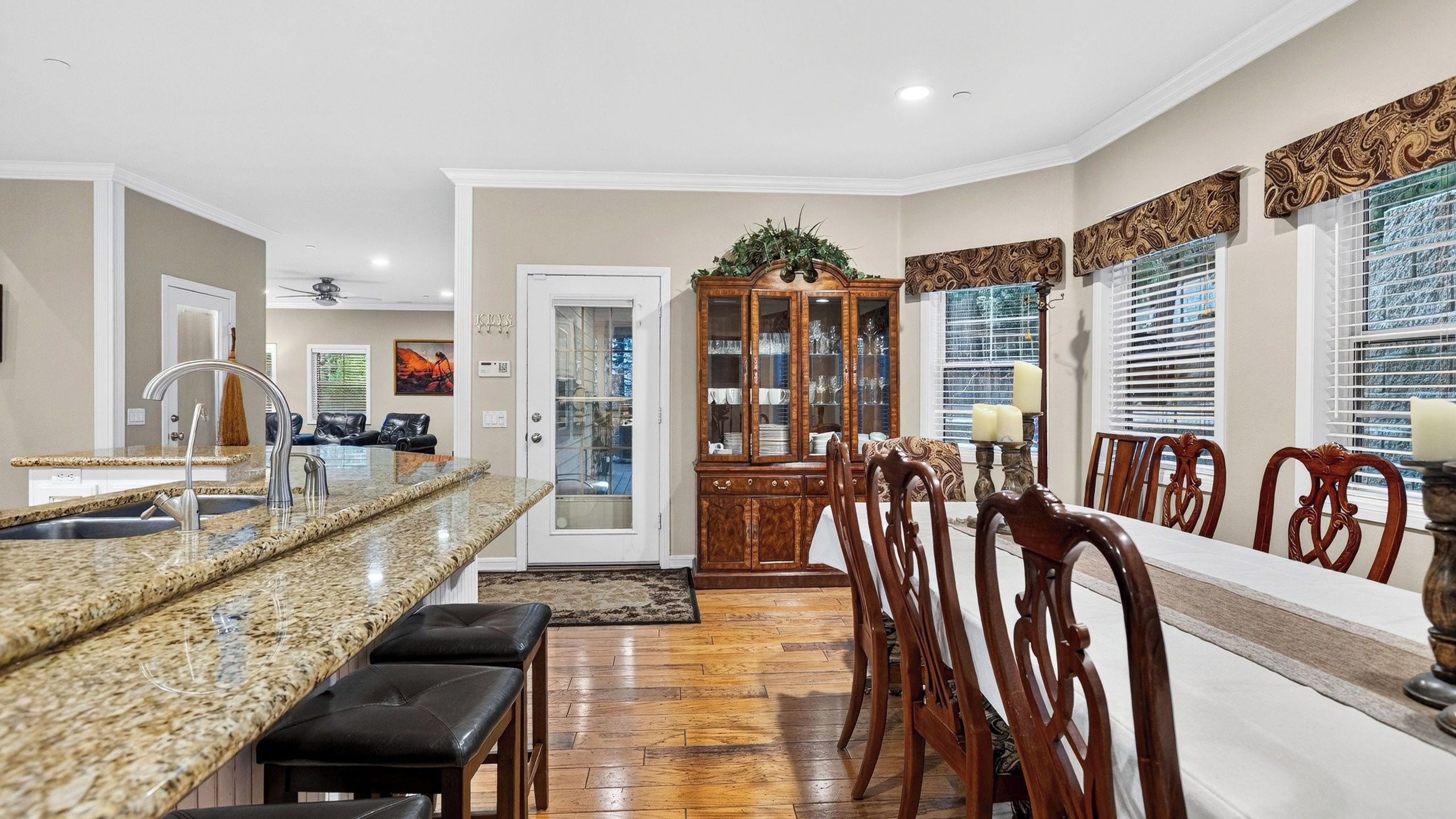 A modern kitchen with a granite countertop, a dining area with wooden chairs, and a glass-fronted cabinet.