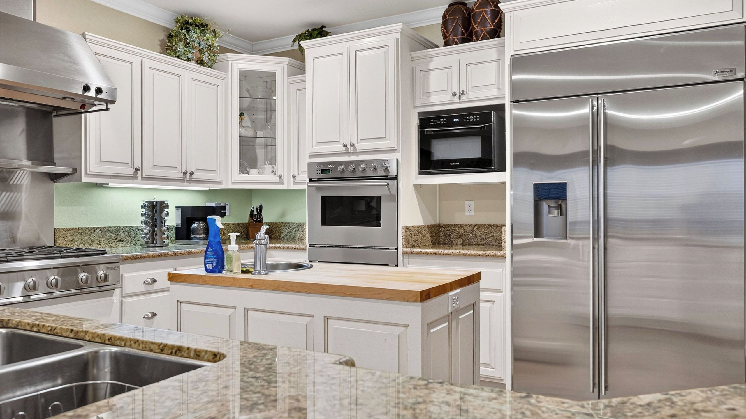 A modern kitchen with stainless steel appliances, white cabinetry, granite countertops, and a built-in oven.