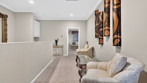 A hallway with a sofa, a glass table, and a chair. There is a door leading to another room. - Wooded Wonder by Avantstay Game Room + Covered Decks + Fire Pit Near Lake Arrowhead (Lake Arrowhead)