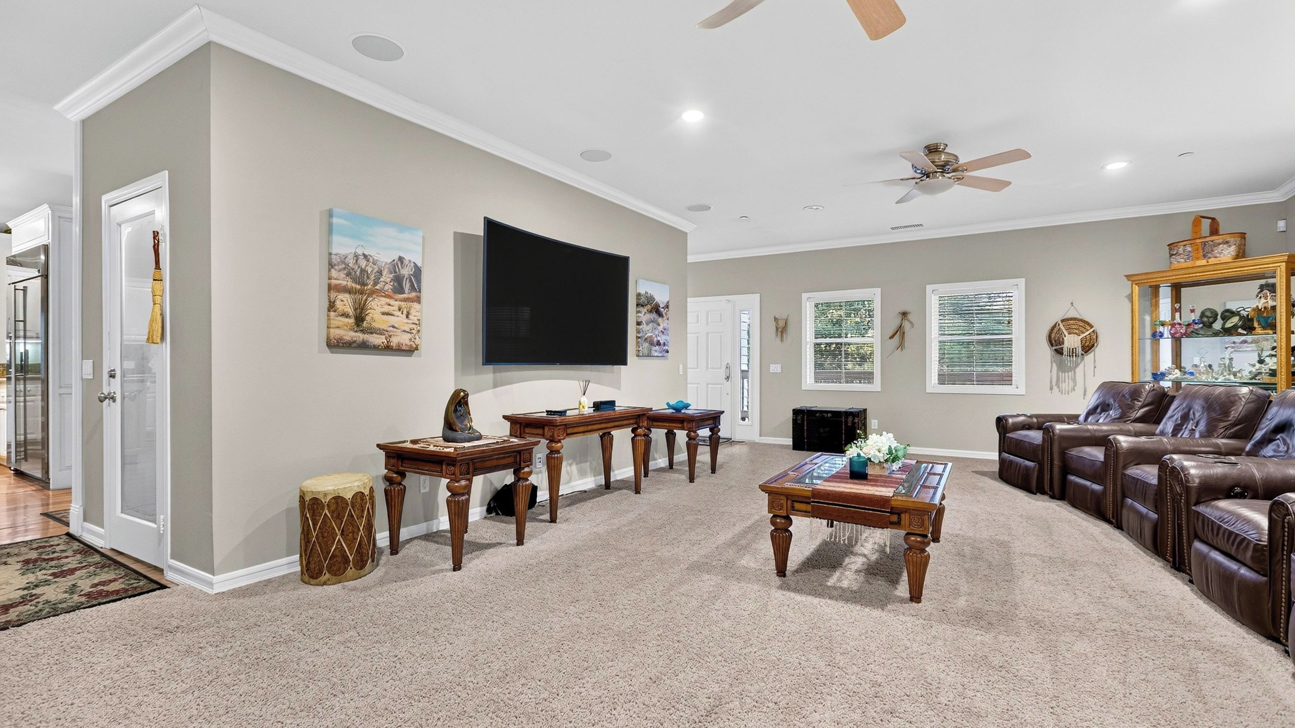 A spacious living room with a flat-screen TV, a fireplace, a leather couch, and a ceiling fan.