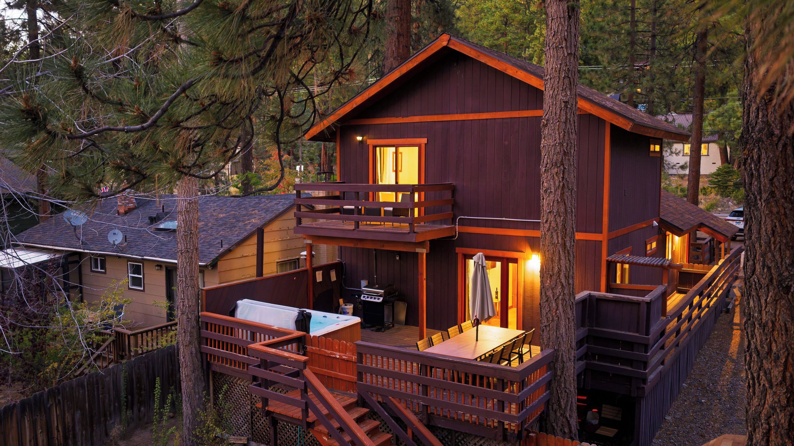 A two-story wooden cabin with a balcony, a hot tub, and a deck.