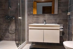 Un baño con cabina de ducha de vidrio, un lavamanos blanco con espejo y un inodoro.