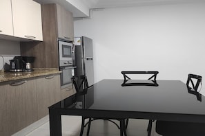 Una cocina moderna con una mesa y sillas negras, horno empotrado y refrigerador.