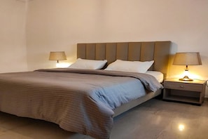 Una cama bien tendida con cabecera, dos lámparas de noche y una mesita de noche con lámpara.