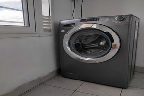 A front-loading washing machine in a corner of a room with a window and a tiled floor. - Cosy Stay . (Tunis)