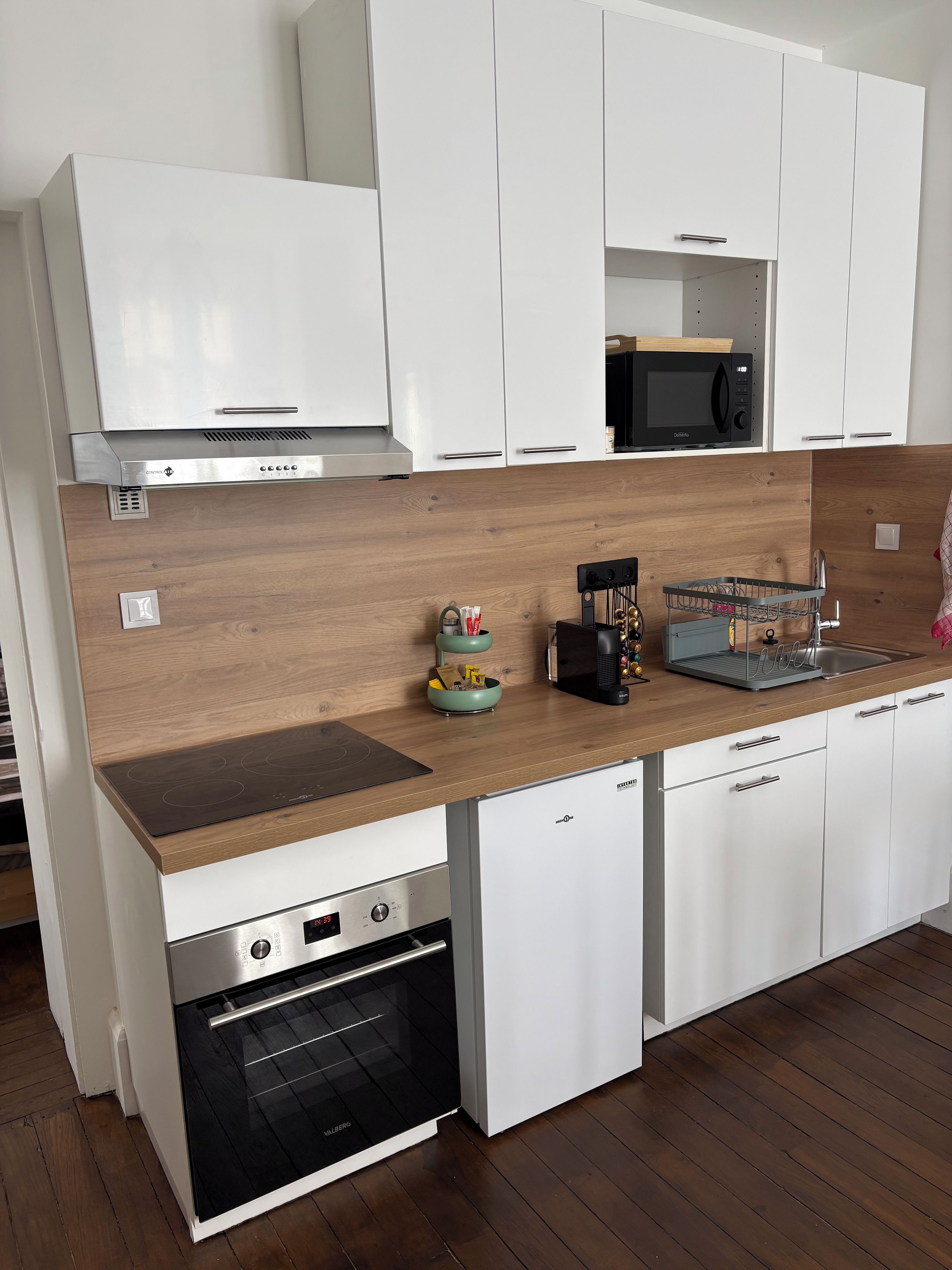 Una cucina moderna con mobili bianchi, un piano di lavoro in legno, un forno integrato e un forno a microonde.