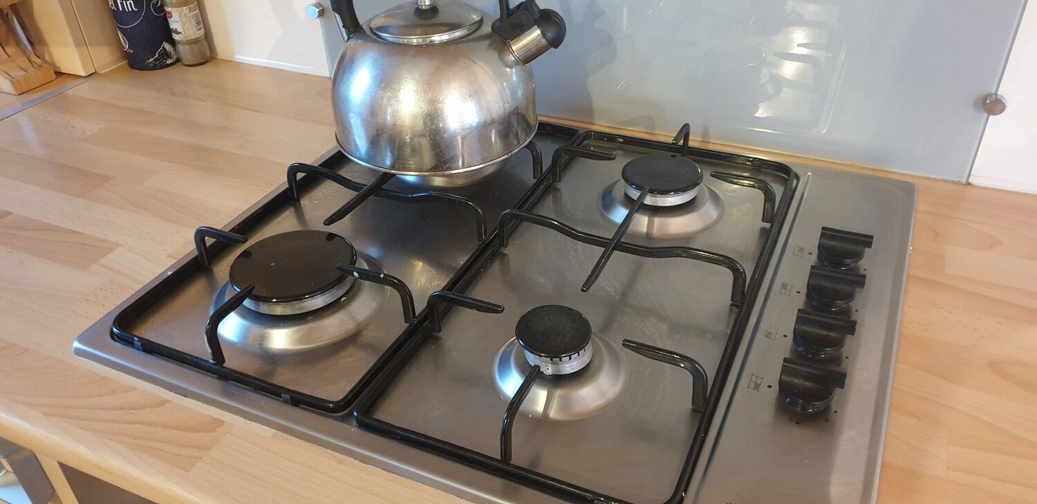 Una cocina con estufa de gas de cuatro quemadores, un hervidor y una olla de acero inoxidable.