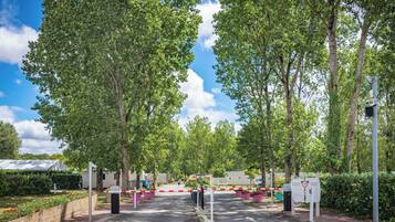 A gated entrance with a pedestrian crossing, surrounded by trees and a clear sky.