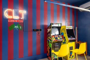 A neon sign reading 'CLT' and 'CORVETTE BLVD' on a striped wall, arcade games, and yellow chairs. - CLT Maison: 5BR Charlotte Retreat with Sauna, Hot Tub, Game Room & Gym (Charlotte)