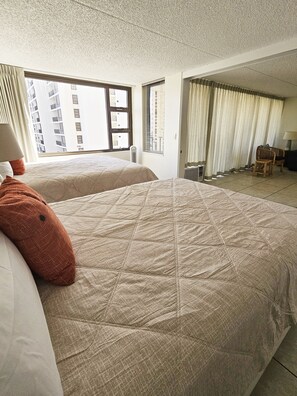 Ein Hotelzimmer mit zwei Betten, Blick auf ein Gebäude und einer Sitzecke mit Stuhl und Tisch.