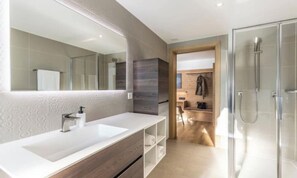 Un baño moderno con un espejo grande, lavamanos doble y ducha con mampara de vidrio.