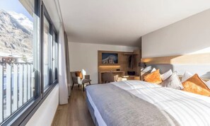 Habitación de hotel con una cama grande, un escritorio y una silla. Se ve una ventana con vistas a las montañas.