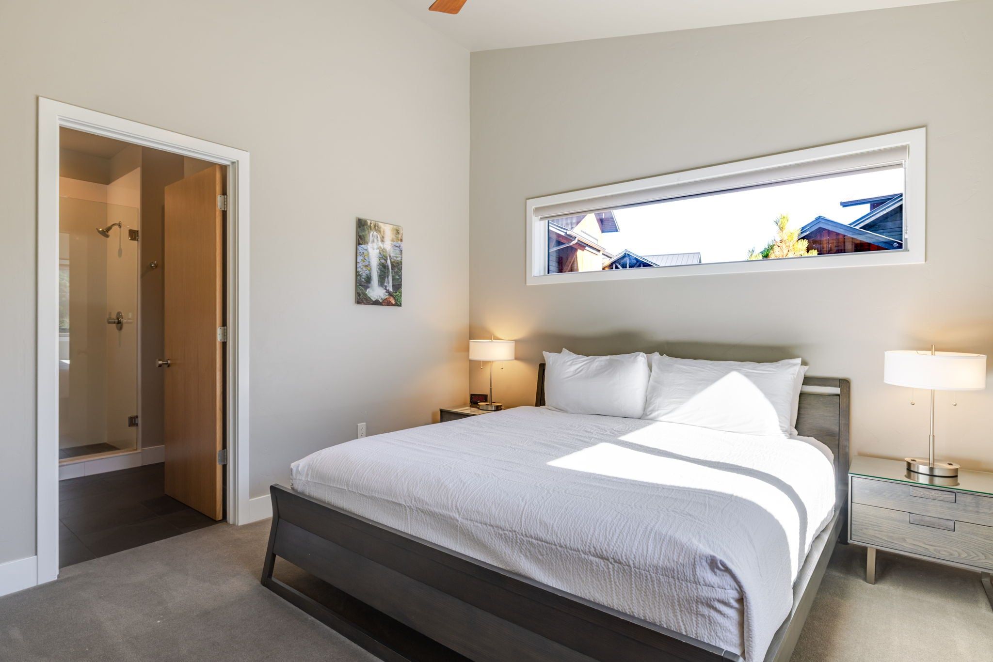 Une chambre à coucher comprenant un lit, des tables de chevet, une fenêtre et une porte donnant sur une salle de bain.