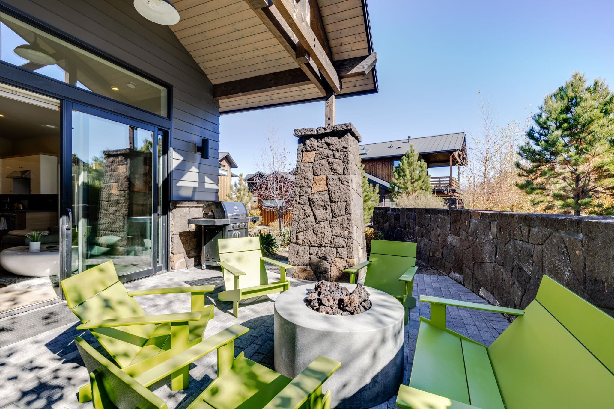 An outdoor patio with green seating, a stone pillar, and a grill.