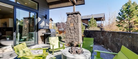 An outdoor patio with green seating, a stone pillar, and a grill.