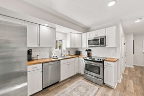 A modern kitchen with stainless steel appliances, white cabinetry, and a wooden countertop. - Loon Mountain Getaway | Game Room + 2 Kitchens (Woodstock)