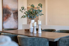 A dining area with a wooden table, grey upholstered chairs, a white vase with green foliage, and two white candle holders. - NEW|The Beaumont @ Bainbridge|Heated Pool|FirePit (Fountain Hills)