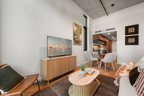 Ein modernes Wohnzimmer mit Flachbildfernseher, einer Holzkommode, einem runden Couchtisch und einem Essbereich mit Stühlen.