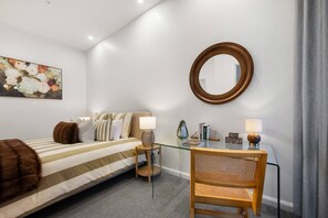 Ein Hotelzimmer mit Bett, Nachttisch, Stuhl und einem an der Wand befestigten Spiegel.