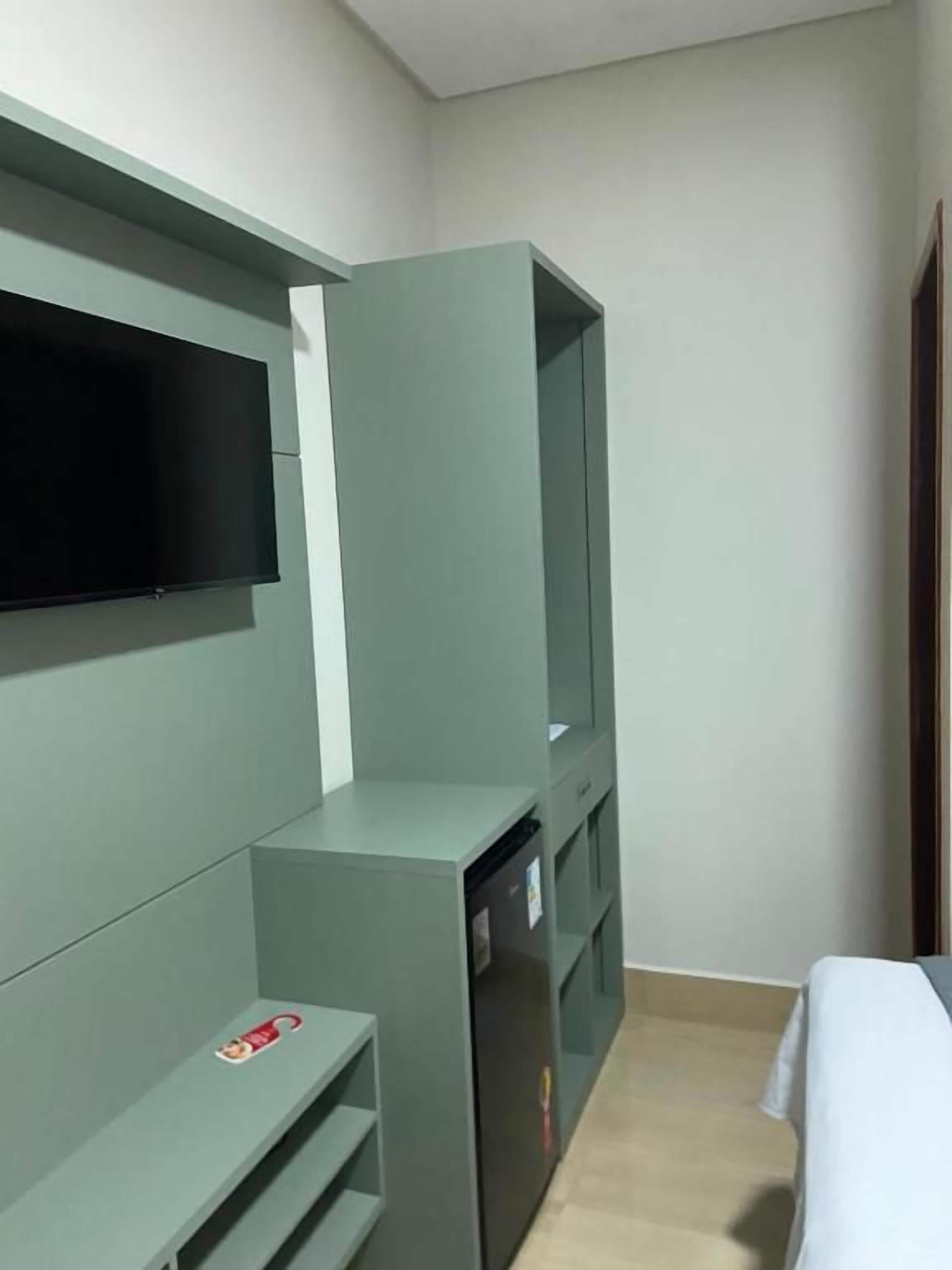 Ein Zimmer mit einem an der Wand befestigten Flachbildfernseher, einer eingebauten Schrankwand und einem Bett mit weißer Bettdecke.