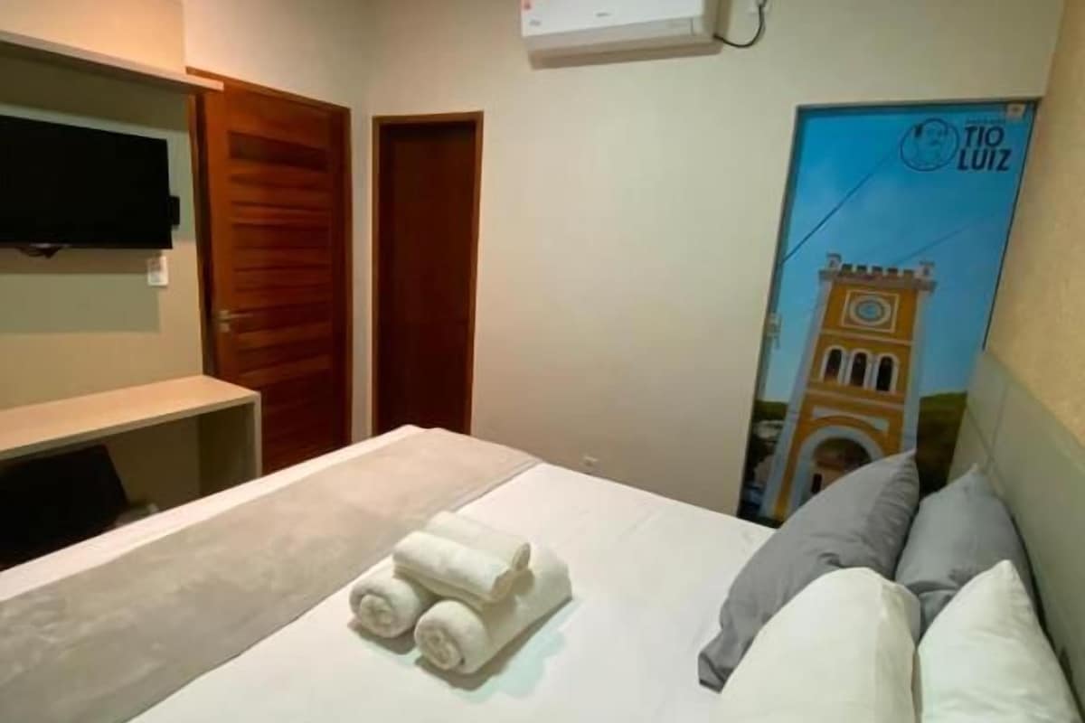 Une chambre d’hôtel équipée d’un lit, d’un téléviseur à écran plat fixé au mur, d’un climatiseur et d’une affiche représentant un bâtiment.