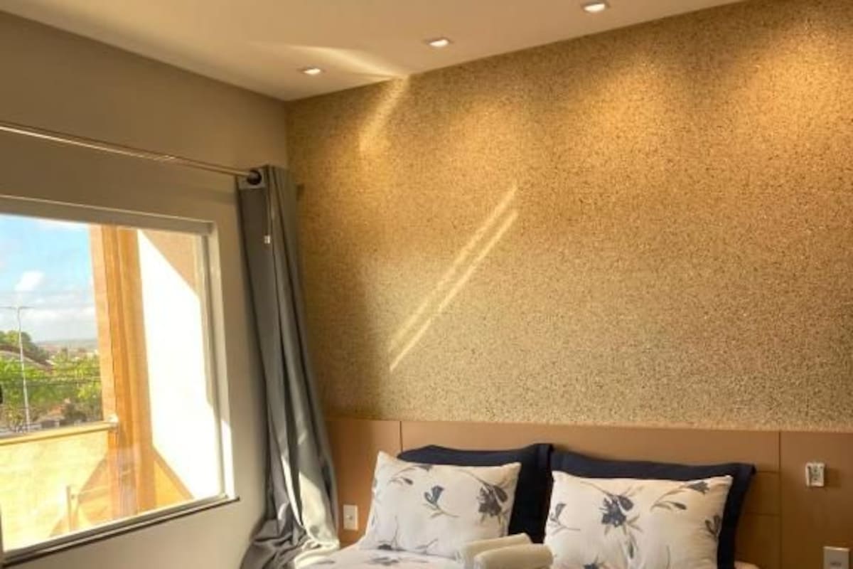 Une chambre d’hôtel avec un grand lit, une vue par la fenêtre et un mur à la texture particulière.