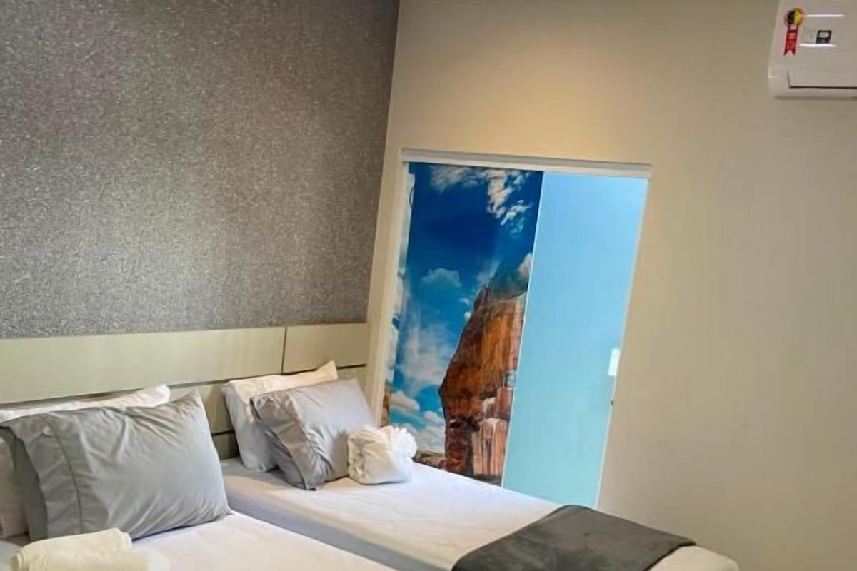 Une chambre d’hôtel avec deux lits, une grande fenêtre et un tableau représentant une montagne.