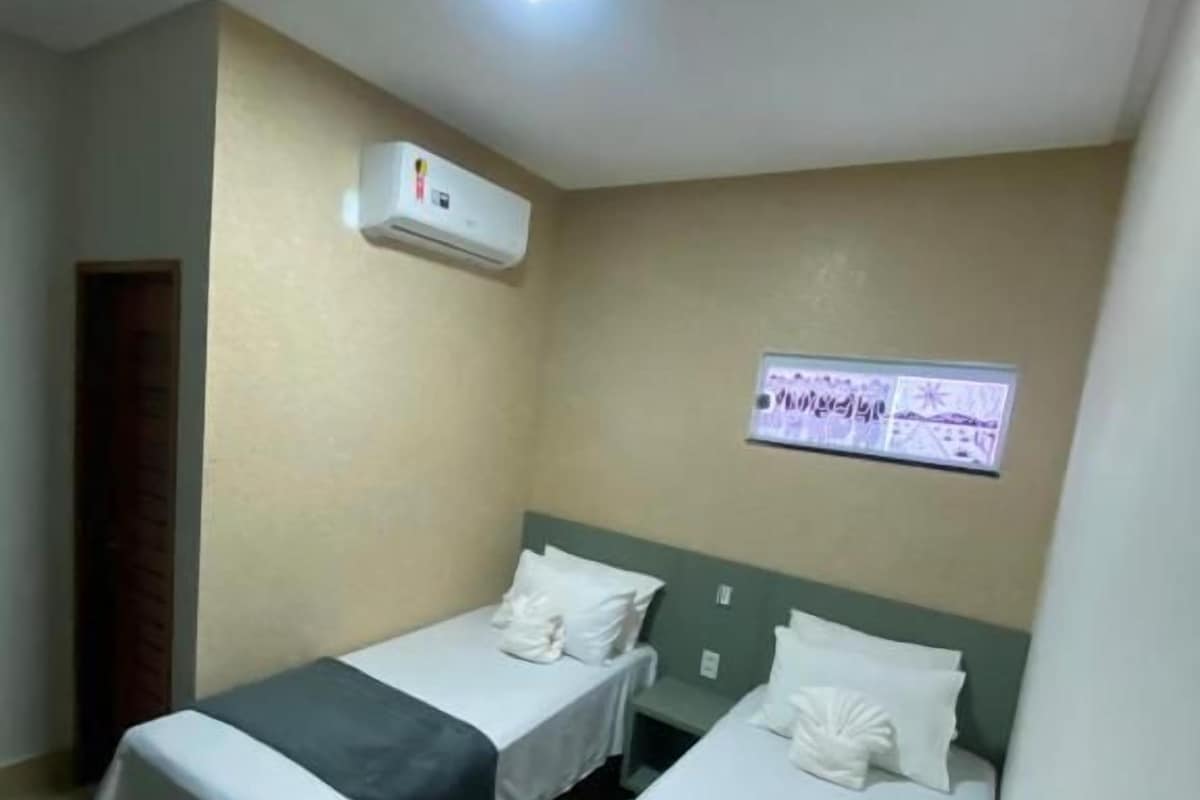 Une chambre d’hôtel avec deux lits simples, un luminaire au plafond, un appareil de climatisation et un panneau fixé au mur.