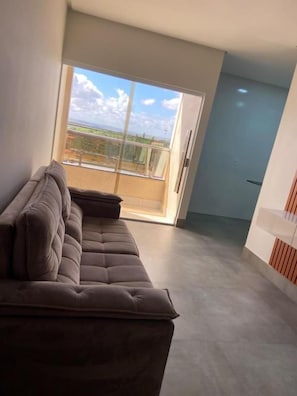 Un salon moderne avec un canapé, une porte-fenêtre coulissante donnant sur un balcon et une porte menant à une autre pièce.